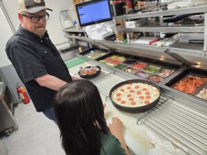 Avalanche Pizza owner helps customer make her pizza