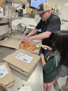 owner of Avalanche Pizza helps a kid make her own pizza